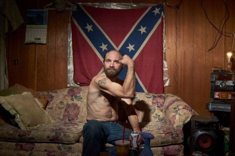 Stacy Kranitz  West Columbia, West Virginia, 2013  Archival Pigment Print  16 x 24 inches, Edition of 7  27 x 40 inches, Edition of 3, Man flexing his bicep in front of a confederate flag, West Virginia