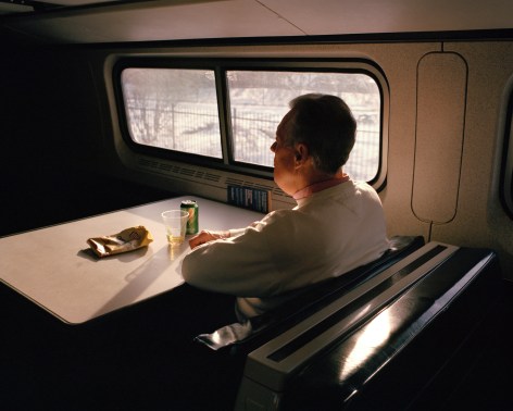 Person seated at table on train, photographed from behind, by McNair Evans