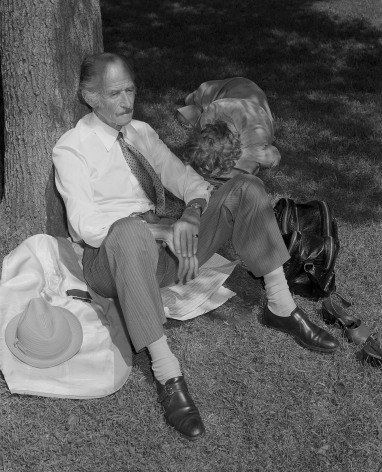Man sitting on newspaper by tree with woman sleeping beside him. Photograph by Mike Smith