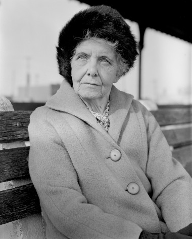 Older, well dress woman in hat, seated. Photo
