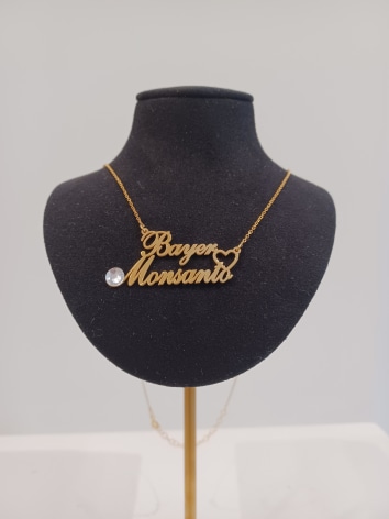 Gold necklace with gem and the text &quot;Bayer Loves Monsanto&quot; on black velvet stand