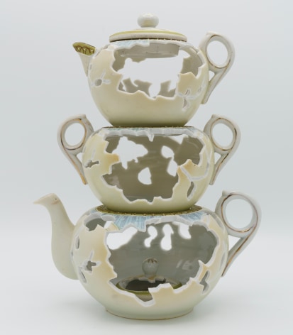 A stack of three tea pots set one on top of the other, the largest on the bottom to the smallest on top. A hand cut holes are in each pot