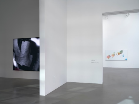 A view of a black and white LED lit piece in a room in the forefront, and another more colorful work in a room farther in the distance.