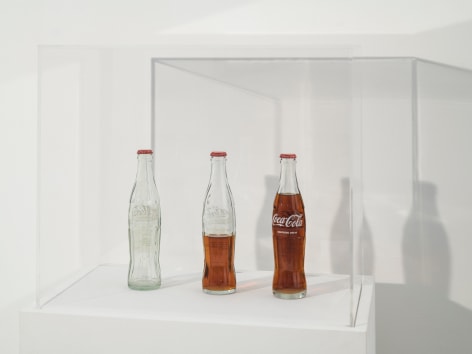 Cildo Meireles, Insertions into Ideological Circuits: Coca Cola Project, 1970-2018. 3 glass bottles, 3 metal caps, liquid, and adhesive labels with text, 53 1/2 x 22 x 14 in (135.9 x 55.9 x 35.6 cm.)&nbsp;