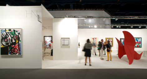 Installation view of Art Basel | Miami Beach 2013, booth B01. This photo displays the booth from afar with a few visitors and features from left to right, two paintings and one large scale sculptures, the first painting on the left is abstract and made by Joan Mir&oacute;, it is called Femmes et Oiseaux dans la nuit, 1968 Oil on canvas 145 x 113 cm. (57 x 44 1/2 in.). The second painting in the middle wall is by Piet Mondrian and is called Komposition II, with Red, 1926 Oil on canvas 50.2 x 51.1 cm. (19 3/4 x 20 1/8 in.) the painting displays a white background, one horizontal black line 4 inches below the top of the canvas and a second horizontal black line one inch above the bottom of the canvas, a third vertical black line crosses those two lines on the left side of the canvas, 4 inches from the left side canvas edge. We can see a large red scale sculpture made of three metal sheet in shapes of loose, curvy, triangles, and four other blurry colorful paintings in the far background made of green, red, purple and yellow tones. Photography by Karen Fuchs.  &copy; 2018 Calder Foundation, New York / Artist Right Society (ARS), New York. &copy;Helly Nahmad Gallery NY.
