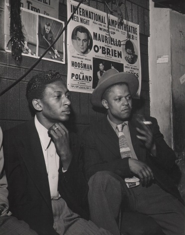 Wayne Miller, Spectators at Pool Hall, Chicago, ​1946&ndash;1947. Two men seated against a brick wall with posters on it, both looking to the right. One man holds a cigarette.