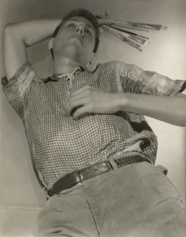 George Platt Lynes, Paul Cadmus, ​c. 1940. Subject is laying down holding paintbrushes above his head.