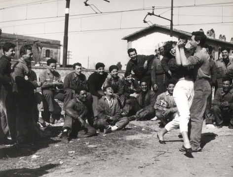 Federico Garolla, Valeria Moriconi - Railway between Rome &amp; Florence, ​1959. A large group of men watch on, smiling, as a couple dances in front of them.