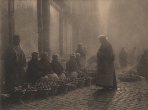07. L&eacute;onard Misonne, Choix difficile, 1933. Older woman stands on a cobbled street facing a row of women seated with baskets of produce. Sepia-toned print.