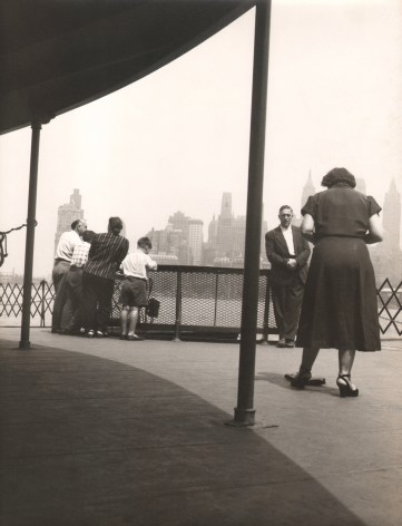 06. Simpson Kalisher, Untitled (Staten Island Ferry), ​c. 1949. Figures standing on a covered pier with a city skyline in the background.