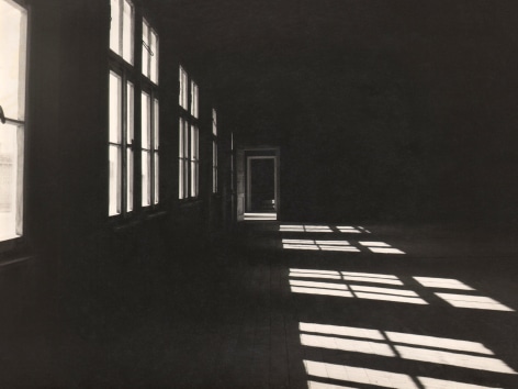 Luciano d'Alessandro, Mauthausen: Il Dormitorio, ​c. 1960. A dark hall with windows along the left casting light onto the floor on the right.