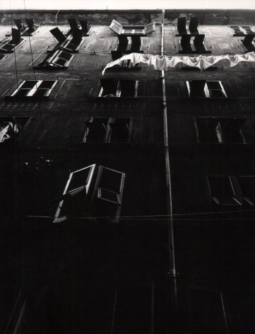 Vittorio Ronconi, Camogli - Le sue case, ​c. 1960. Dark scene looking up at columns of windows of an apartment building. A laundry line hangs across the upper right holding white fabric.