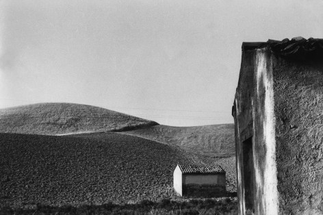 10. Frank Monaco, The buildings were once cottages of people who have emigrated, c. 1966. Hilly landscape and two one-room structures in the right foreground.