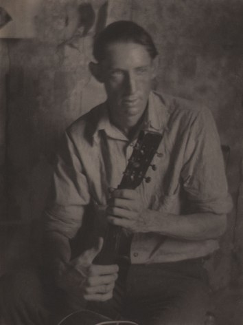 Doris Ulmann, Untitled (Guitar player), ​1928&ndash;1934. Seated man holding the neck of a guitar in both hands. His face is slightly blurred with motion.