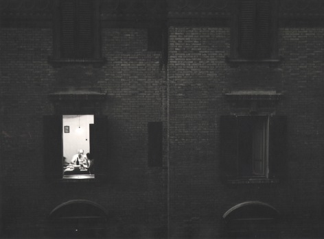 Nino Migliori, Summer evening from 'People of Emilia,' 1953. Exterior view of an apartment building. One window is lit and a family is seated at the dinner table.