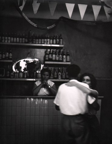 Piergiorgio Branzi, Firenze, Ballo alla casa del popolo di San Frediano, ​1959. A couple dances in the foreground with a woman looking on from behind the bar in the background.
