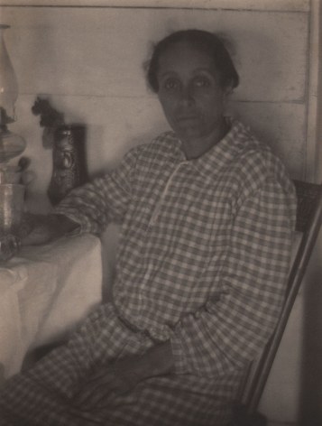 Doris Ulmann, Untitled (Appalachian woman), ​1928&ndash;1934. Woman in a checkered dress seated at a table and looking to the camera. One hand is in her lap, the other rests on the table by a drinking glass.