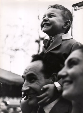 Mario Cattaneo, Untitled, ​c. 1960. A young boy sits on a man's shoulders, holding on to his face. A woman's face is out of focus in the foreground. All are smiling and looking to the left of the frame.