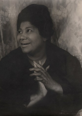 08. Carl Van Vechten, Mahalia Jackson, 1962. Bust-length portrait with subject smiling towards the upper left of the frame with hands clasped at her chest.