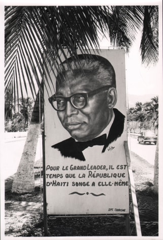 08. Graham Finlayson, Haiti - Crude posters like this one - all of them extolling Duvalier for near-divine virtues, are emblazoned all along the main seafront road in Port au Prince, c. 1958&ndash;1966. A poster with a portrait of a man and the words &quot;pour le grand leader, il est temps que la R&eacute;publique d'Haiti songe a elle-m&ecirc;me&quot;