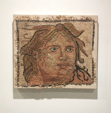 A mosaic depicting the head of a man with flowing hair and comprised of small marble and volcanic stone tesserae in earth tones in a square format
