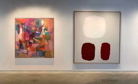 A painting by Ray Parker comprised of rose, green, yellow, blue, purple, and white strokes of color to the left of a painting by Ray Parker comprised of three forms in white maroon and umber on a grey ground