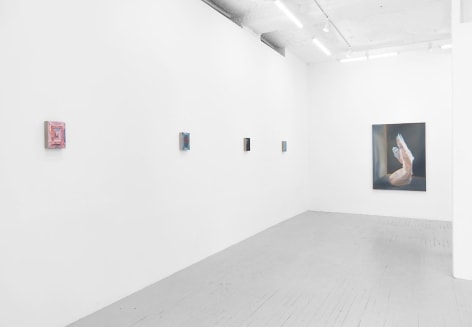 A photograph of 4 small paintings on the wall at left, detail indiscernible, and one large painting on the back wall of a kneeling naked woman seemingly made out of cellophane, looking at a wall.