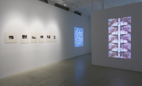 Two videos by Luther price, one on the foreground projected onto a temporary wall and the other is on the wall at left in the gallery. Additionally, the wall at left has 6 black and white photographs by Herv&eacute; Guibert in cream mattes.