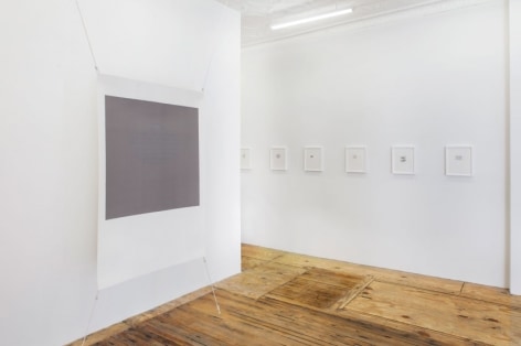 A photograph of the threshold to the back office where we see one gray screenprint, and a row of smaller works framed in white.