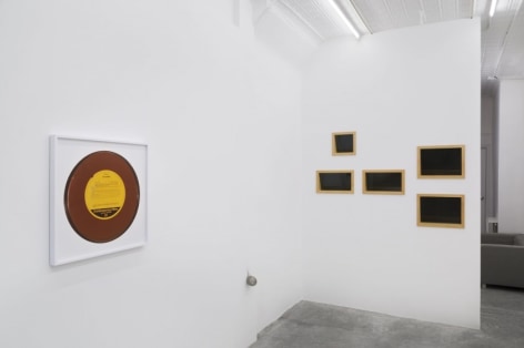 A photograph of the gallery, with a framed record at left and 5 rectangles on the back wall at right.
