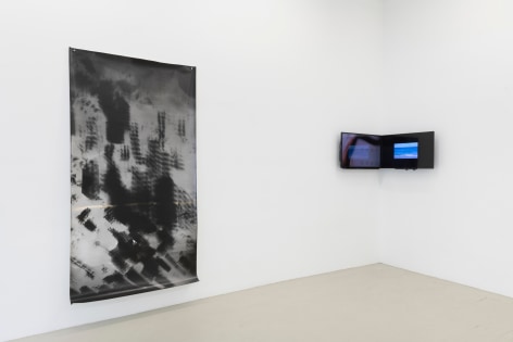 an installation view of the show showing the large photogram and a video installation of two monitors installed to a corner of the gallery, edge to edge