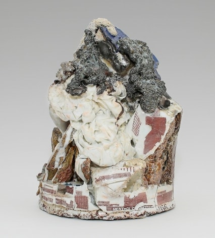 A mixed ceramic sculpture with a round base that moves to an apex. At the peak of the small sculpture is a silver volcanic mass, beneath which is a ceramic piece that resembles a crumbles bedsheet. Near and beneath the white mass is stone with decals (lottery numbers, cigarette logos) applied in red.