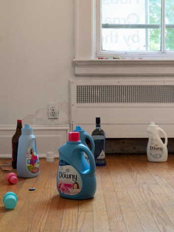 A close-up photograph of detergent bottles and liquor bottles on the ground in front of a window