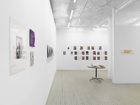 A photograph of the long line down the length of the gallery. The artwork on the back wall of magazine spreads is visible alongside a table in the middle of the room At left is a single photograph by Guibert and 2 drawings by Ettinger.