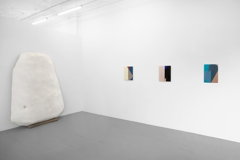 A photograph of the front half of the gallery with three enamel on steel paintings and one large white sculpture leaning against the temporary wall in the gallery.