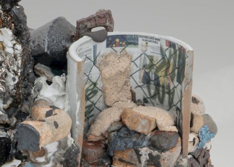 A detail of a mixed stoneware sculpture that introduces us to decals on the backside of a circular shape. There is a chainlink fence overlay, and we see newspaper press clips collaged together. There are also varies textures of clay in black, beige, silver, and white.