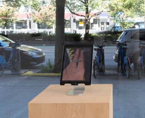 an iPAD on a stand placed on a pedestal. The iPAD has a still from the video. The image shows a person holding a smart phone