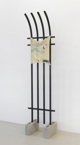a sculpture comprised of a piece of vertical bar fencing embedded in two concrete blocks. A yellow piece of fabric, actually made from glass, hangs from the fencing