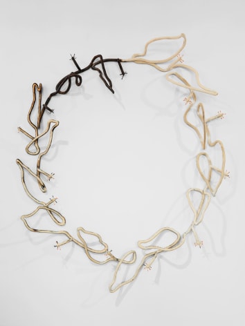 An abstracted wreath mounted on the wall, made of plywood to resemble a single line. One-quarter of the wood is burned and black, which gradually shifts to untarnished plywood as you move around the wreath