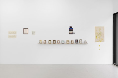 An installation view, on the wall is a sculpture made up of old cigarette cartons on a shelf, and 4 other drawings on paper without frames.