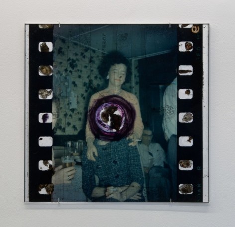 An enlarged film still with a woman in the center, and a hole burned in the center surrounded by purple ink.