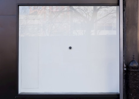 A photograph of the exterior of the gallery, which depicts a small camera situated on a white wall behind the glass of the gallery's facade.