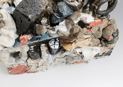 A close up detail image of a mixed stoneware sculpture. We see an assortment of textures: gold luster, blue enamel, red enamel, blue luster, cracked pieces of porcelain that appear to congeal together, sandy masses, and bubbles upon the surface. It is a jagged construction.