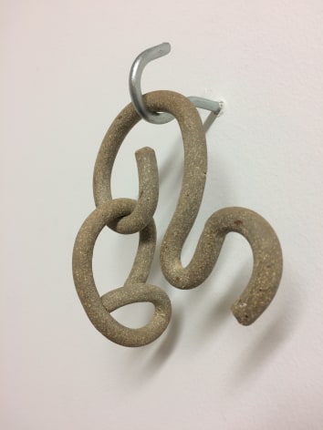 A stoneware artwork hanging from a hook, that appears like a noodle contorted