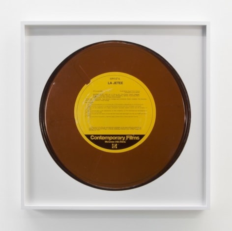 A framed print of a record, which is brown with a yellow center and illegible text.