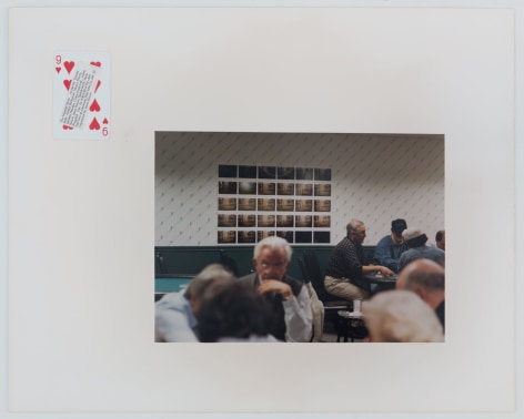 A photograph of elderly men in a card hall with a grid of photographs behind them. The photograph is presented on a mount with a 9 of Hearts playing card at top-left