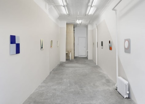 A photograph of the gallery, with enamel paintings on both walls in a single row. The left wall is grey, right wall have a gray slice.