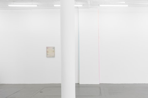 A photograph of the gallery's interior with a white pole in the foreground: to the left is a pale painting by Monick, and at right are two ribbon artworks (blue, pink)