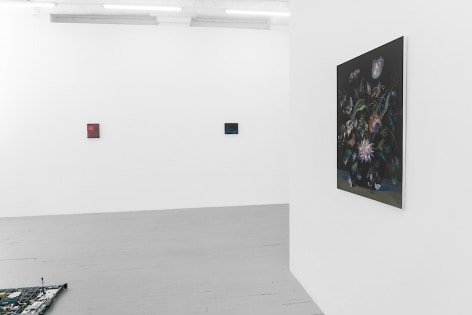 A photograph of the gallery from the side of the temporary wall. There is a floral still life at-right, and on the far wall are two small abstract paintings.