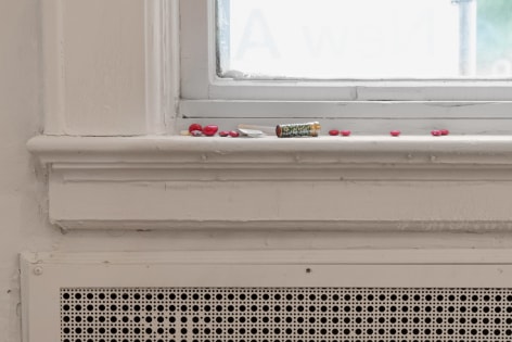 A close up photograph of the window sill with lipstick, red M&amp;Ms, and illegible packs of over-the-counter drugs